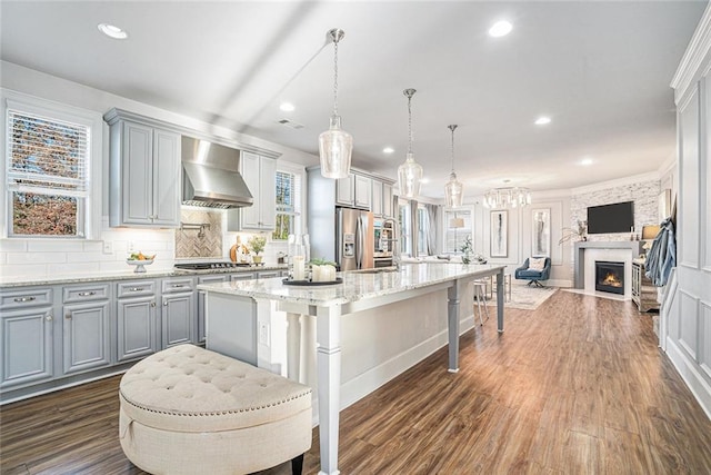 kitchen with a kitchen breakfast bar, wall chimney exhaust hood, dark wood-type flooring, a center island, and hanging light fixtures