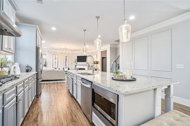 kitchen with dark wood-type flooring, a large island with sink, sink, range hood, and decorative light fixtures