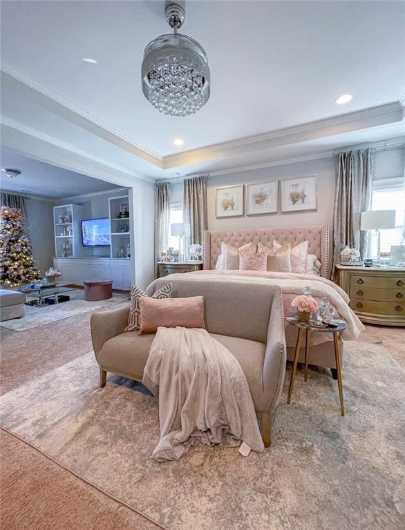 carpeted bedroom featuring a raised ceiling, multiple windows, and crown molding