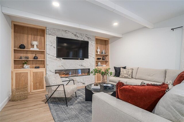 living room featuring a fireplace, beamed ceiling, and light wood-type flooring