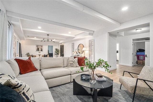 living room featuring beam ceiling, light wood-type flooring, and a chandelier