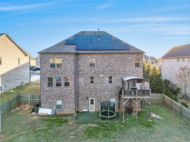 back of house with a lawn, solar panels, a trampoline, and central AC