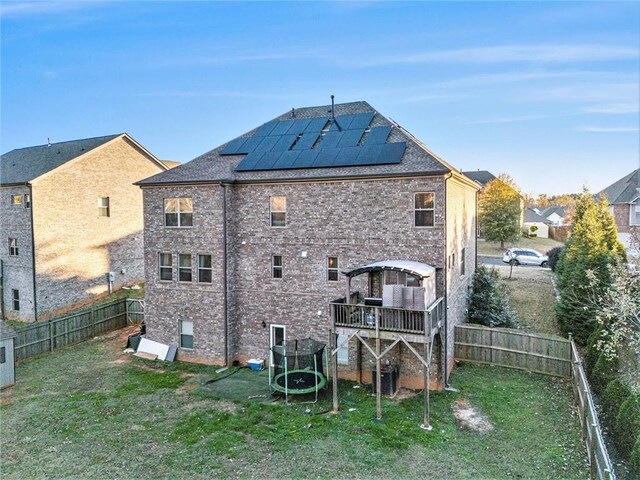 back of house featuring a lawn, a trampoline, and solar panels