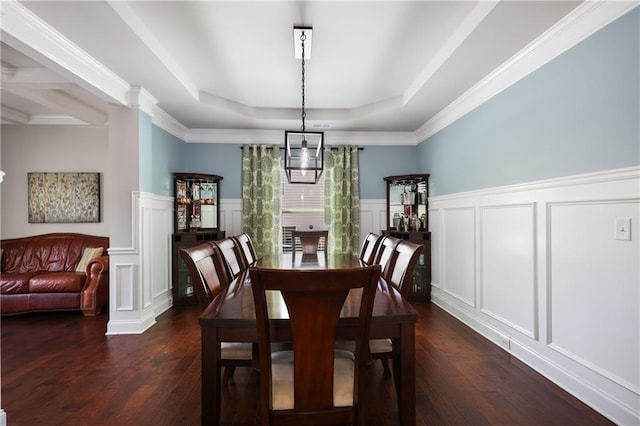 dining space featuring decorative columns, a decorative wall, a tray ceiling, dark wood finished floors, and wainscoting