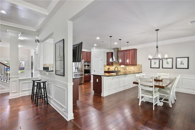 kitchen featuring a peninsula, a sink, wall chimney range hood, a breakfast bar, and a decorative wall