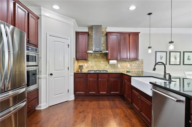 kitchen with appliances with stainless steel finishes, wall chimney exhaust hood, reddish brown cabinets, a sink, and crown molding