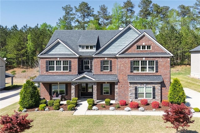 craftsman house featuring covered porch, a front yard, brick siding, and a chimney