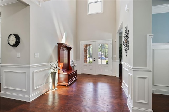 entryway featuring a decorative wall, wainscoting, dark wood-style flooring, a towering ceiling, and french doors