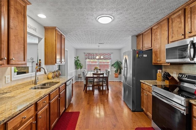 kitchen featuring sink, light hardwood / wood-style flooring, pendant lighting, stainless steel appliances, and backsplash