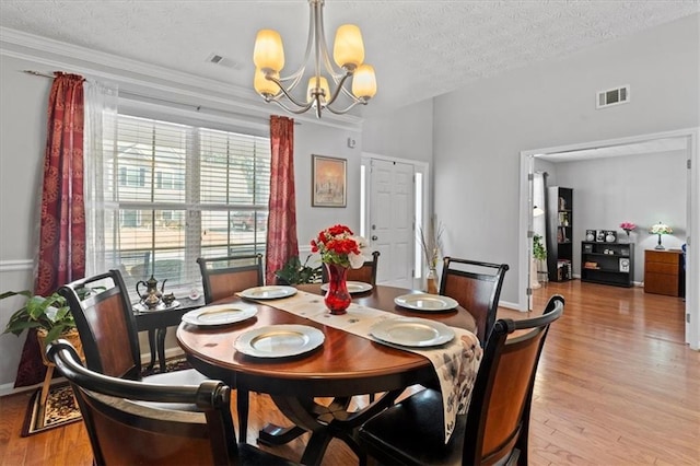 dining area with a textured ceiling, light hardwood / wood-style floors, and a chandelier