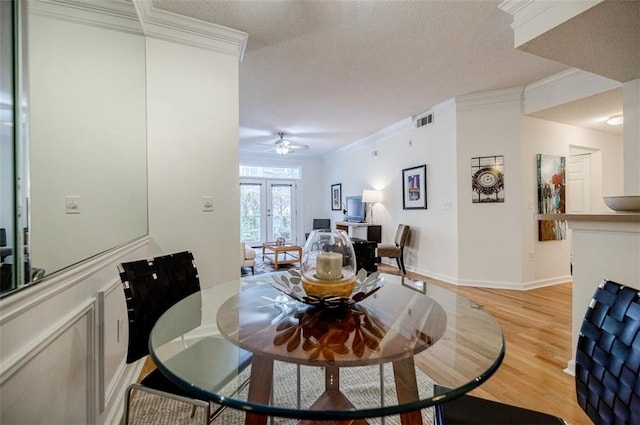 dining room with visible vents, light wood-style flooring, ornamental molding, a textured ceiling, and baseboards