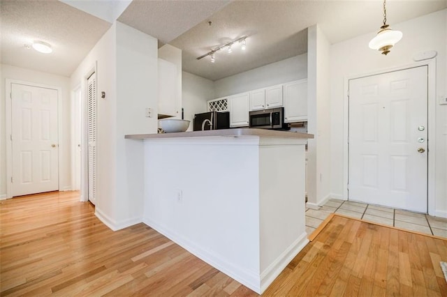 kitchen with a peninsula, white cabinets, freestanding refrigerator, stainless steel microwave, and decorative light fixtures