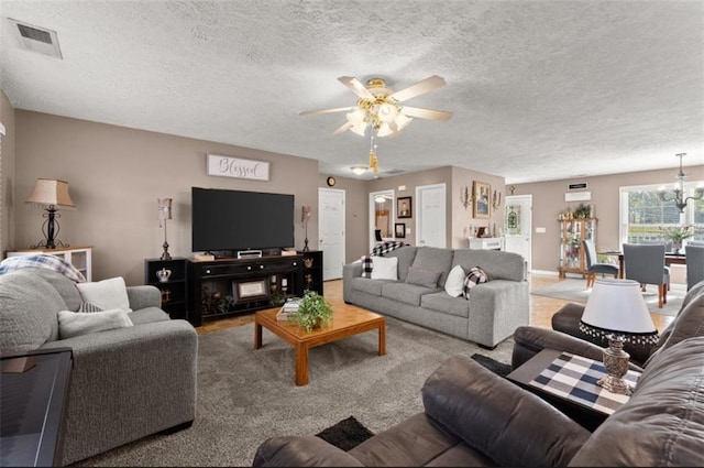 carpeted living room featuring visible vents, a textured ceiling, baseboards, and ceiling fan with notable chandelier