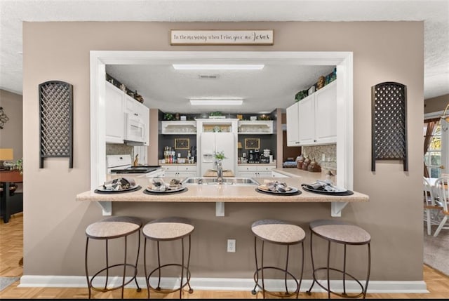 kitchen with a peninsula, white appliances, tasteful backsplash, and white cabinets