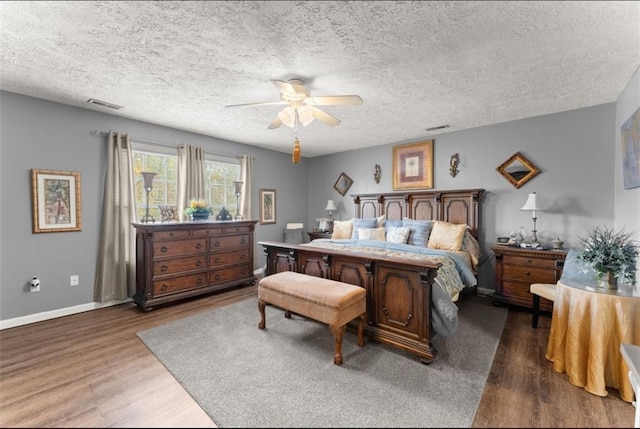 bedroom with visible vents, a textured ceiling, baseboards, and wood finished floors