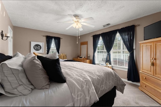 bedroom featuring ceiling fan, visible vents, a textured ceiling, and light colored carpet