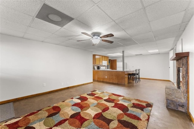 unfurnished living room with a paneled ceiling, a fireplace with raised hearth, finished concrete floors, ceiling fan, and baseboards