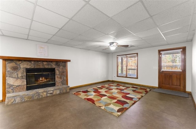 unfurnished living room featuring concrete flooring, a fireplace, a paneled ceiling, and baseboards