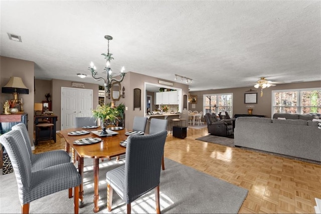 dining area featuring a textured ceiling, a wealth of natural light, ceiling fan with notable chandelier, and visible vents