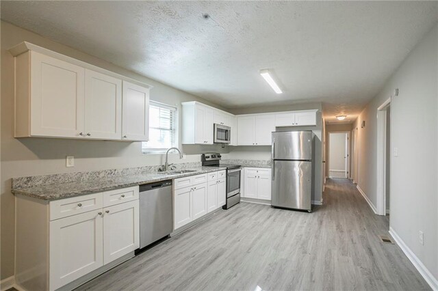 kitchen with sink, light hardwood / wood-style flooring, appliances with stainless steel finishes, light stone counters, and white cabinetry