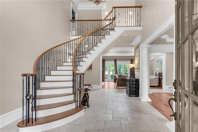 foyer featuring stone tile floors, a towering ceiling, baseboards, ornamental molding, and decorative columns