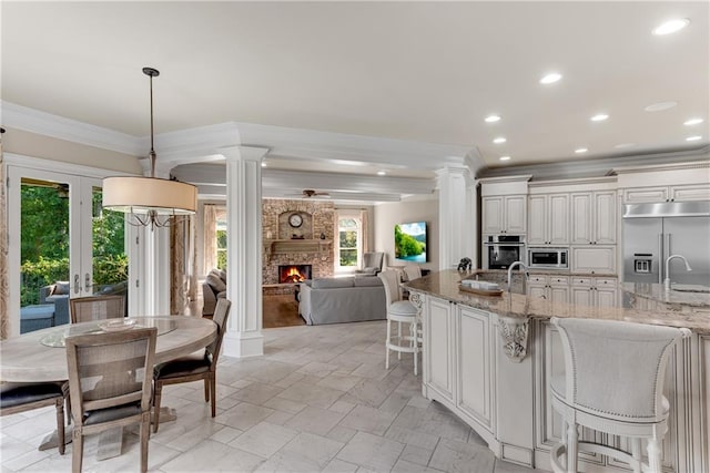 kitchen featuring built in appliances, a fireplace, decorative columns, a breakfast bar, and hanging light fixtures