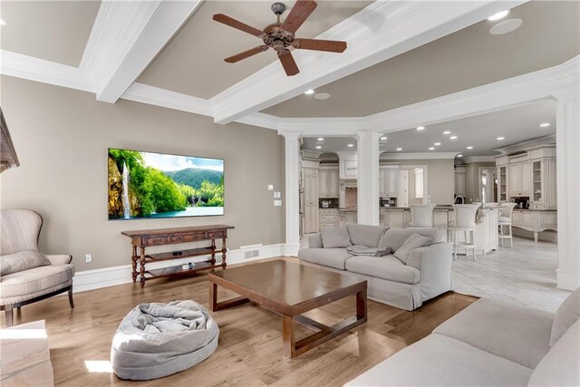 living room featuring light hardwood / wood-style flooring, beam ceiling, ornate columns, crown molding, and ceiling fan