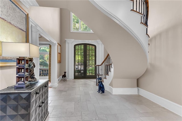 foyer entrance featuring a towering ceiling, stairs, stone tile flooring, french doors, and ornate columns