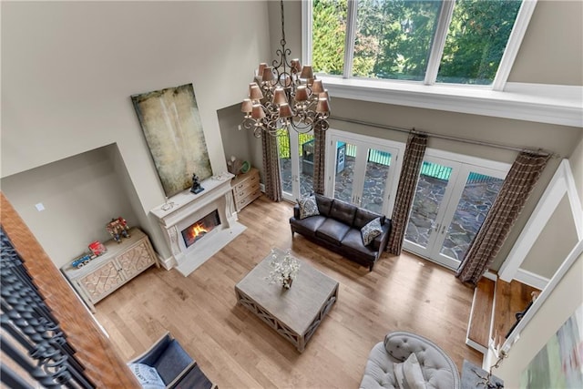 living area featuring french doors, a high ceiling, wood finished floors, a chandelier, and a warm lit fireplace