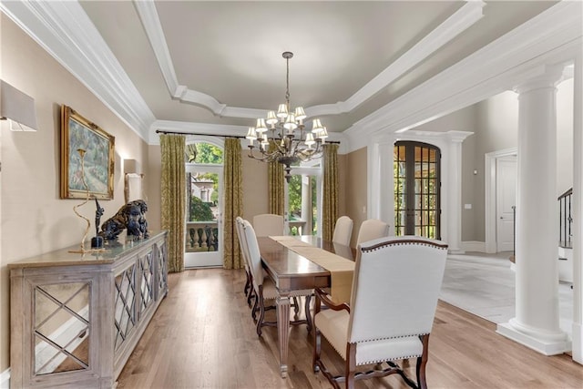 dining space with a raised ceiling, ornate columns, a notable chandelier, and light hardwood / wood-style floors