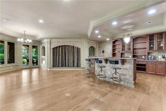 kitchen featuring ornamental molding, decorative light fixtures, a kitchen breakfast bar, stone countertops, and light hardwood / wood-style floors