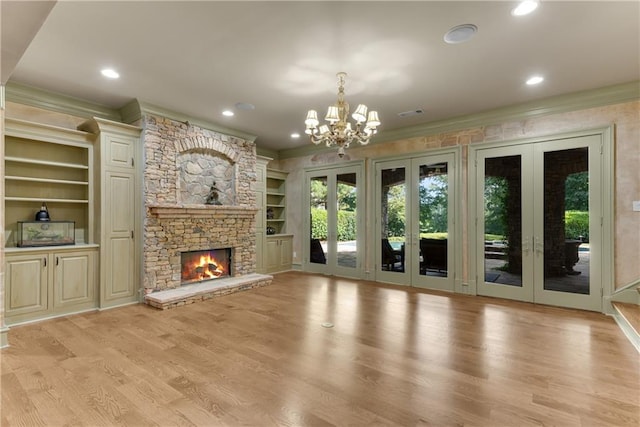 unfurnished living room featuring a fireplace, light hardwood / wood-style flooring, french doors, a chandelier, and ornamental molding