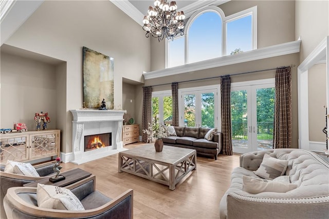 living room featuring light wood-style flooring, a notable chandelier, a lit fireplace, and a high ceiling