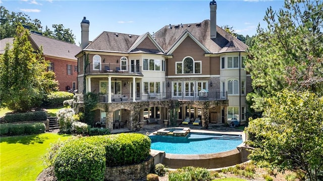 rear view of property featuring an in ground hot tub, a patio, a chimney, and a balcony