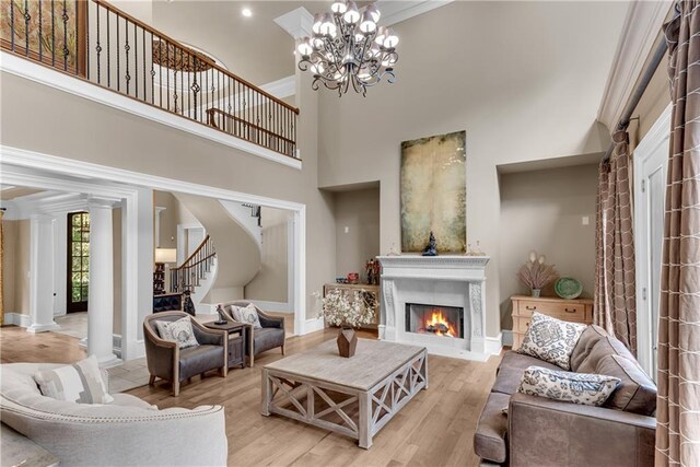 living room with a notable chandelier, crown molding, light hardwood / wood-style flooring, a towering ceiling, and ornate columns