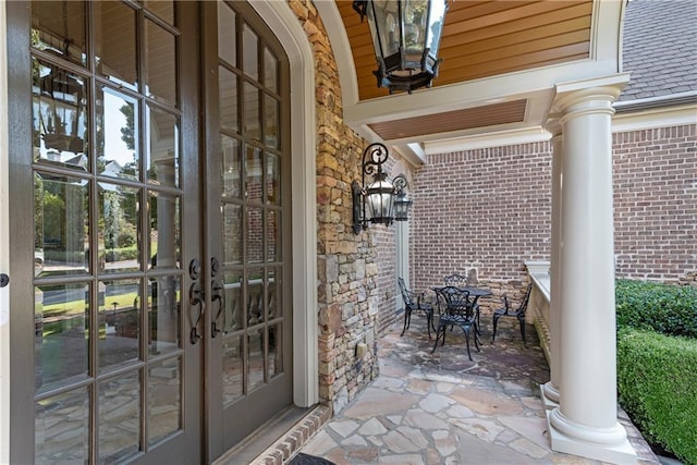 entrance to property featuring a shingled roof, outdoor dining area, french doors, and brick siding