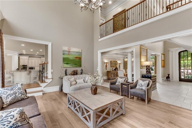 living room with light wood-type flooring, a towering ceiling, crown molding, and ornate columns