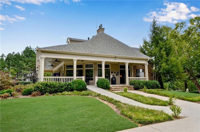 back of property with a porch, roof with shingles, a lawn, and a chimney