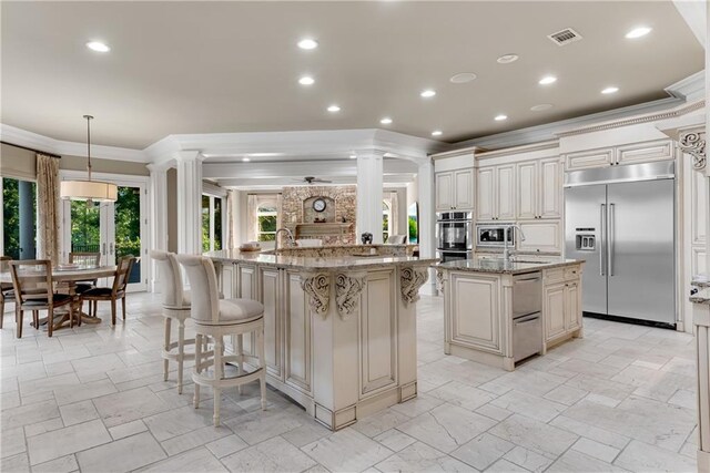 kitchen featuring a large island with sink, ornamental molding, built in appliances, a kitchen bar, and light stone countertops