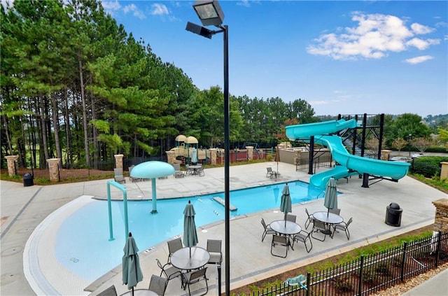 pool featuring a water slide, a water play area, fence, and a patio