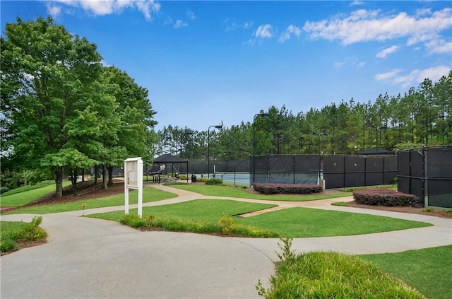 view of property's community featuring a tennis court, a lawn, and fence