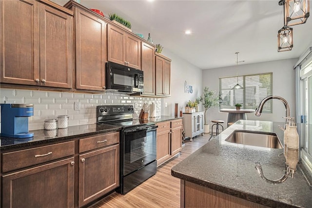 kitchen with hanging light fixtures, light hardwood / wood-style floors, an island with sink, black appliances, and sink