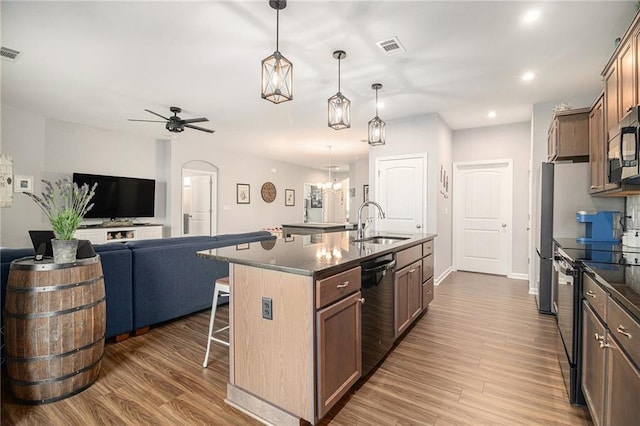 kitchen featuring ceiling fan with notable chandelier, stainless steel appliances, a kitchen island with sink, hardwood / wood-style floors, and sink