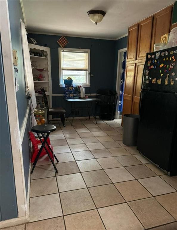 kitchen featuring ornamental molding, brown cabinetry, light tile patterned flooring, and freestanding refrigerator