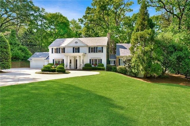 view of front of house with concrete driveway, a front yard, a garage, and a chimney