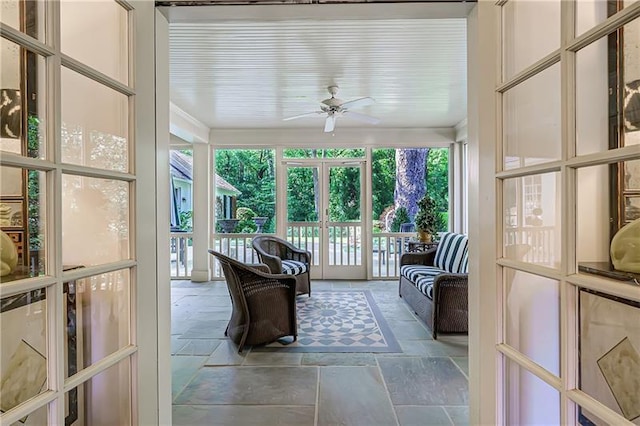 sunroom with stone tile floors and ceiling fan