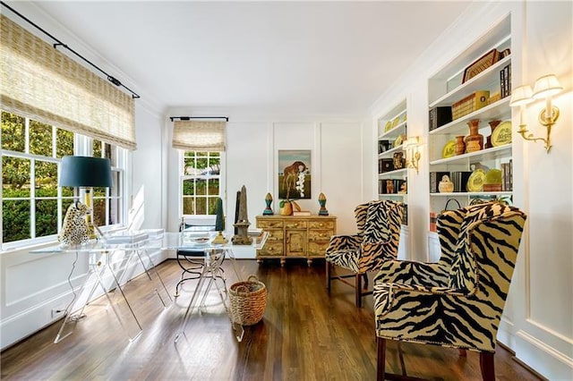 living area featuring wood finished floors, a decorative wall, built in shelves, and crown molding