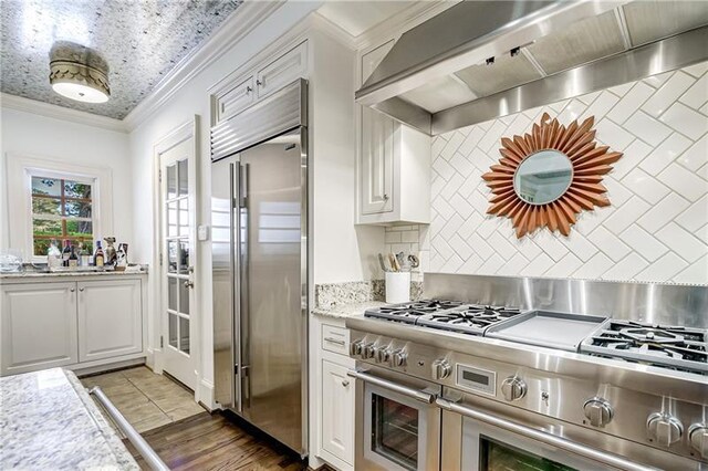 kitchen with premium appliances, custom exhaust hood, backsplash, white cabinets, and crown molding