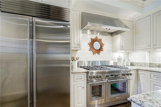 kitchen featuring high quality appliances, wall chimney range hood, white cabinets, and ornamental molding