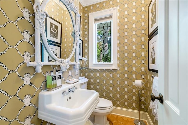 bathroom with toilet, wallpapered walls, a sink, and crown molding